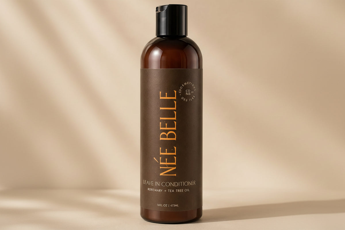A bottle of Née Belle Leave-In Conditioner with Rosemary and Tea Tree Oil, featuring an amber brown bottle and a dark brown label with gold lettering, set against a warm beige background with soft shadow overlays.